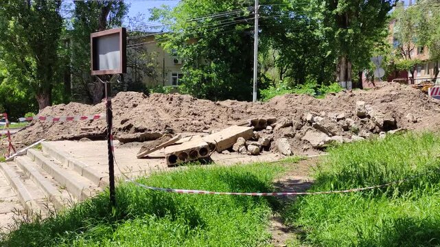 Dirt pile and construction debris with red and white warning tape on sidewalk