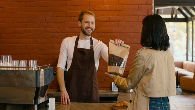 Barista hands coffee bag to customer in cozy cafe interior