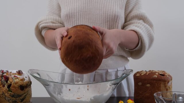 Woman dipping panettone into white icing and decorating Easter bread with colorful holiday sprinkles
