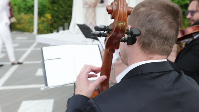 Over the shoulder view of a cellist playing classical instrument with string quartet outdoors