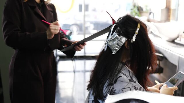 A master hairdresser lightens the hair strands of a client with long hair. Hair coloring in a model with long black hair.