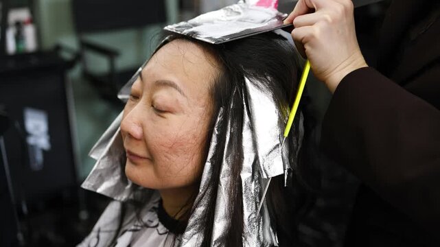 A master hairdresser lightens the hair strands of a client with long hair. Hair coloring in a model with long black hair.