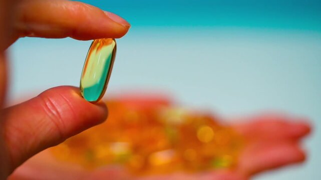 Hand of woman, girl holds golden capsule with Omega 3 on light background. Vitamins