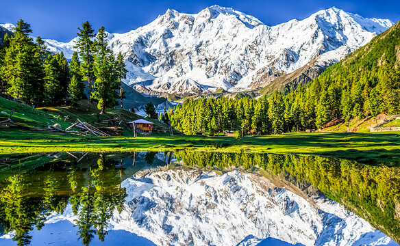 A breathtaking mountain landscape featuring a crystal-clear alpine lake reflecting the majestic summit of Nanga Parbat, the world's ninth-highest mountain, beneath a vibrant blue sky