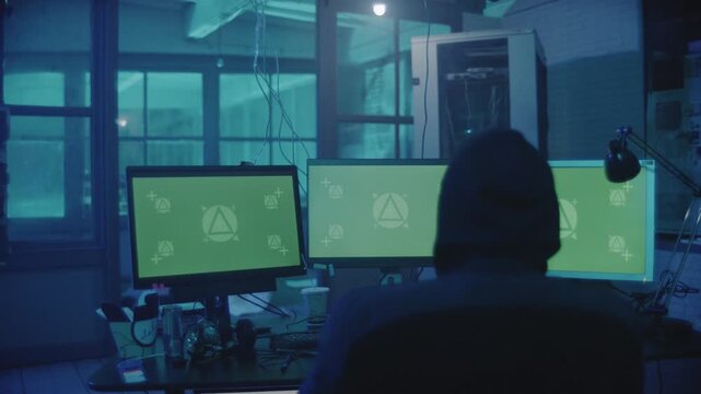 Man in the hood from his back sitting and working at the computer as haker. Hideout Place has Dark Atmosphere.