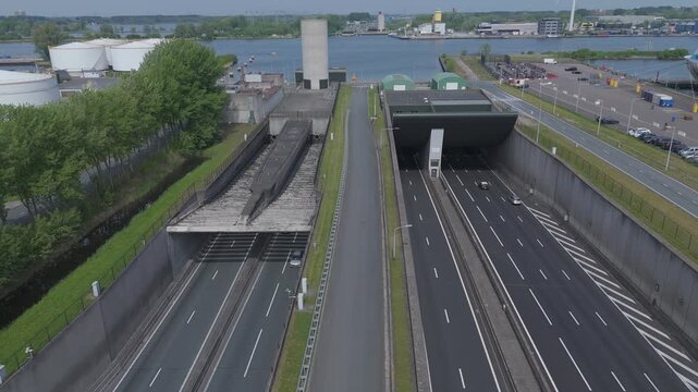 Aerial drone footage above the A10 with a clear view of the Coentunnel entrance and the IJ in Amsterdam. Traffic, harbor infrastructure and waterfront surroundings are visible from above.