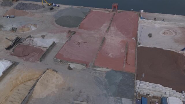 Aerial drone footage flying around an industrial storage yard with bulk materials, stockpiles, conveyors and harbor infrastructure. Large-scale logistics and material handling facility viewed from abo
