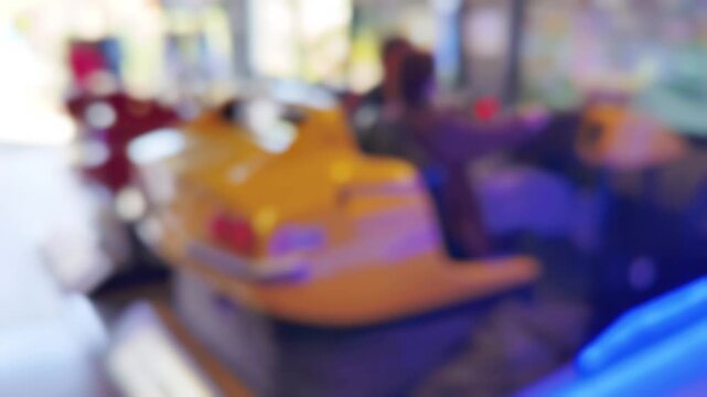 Defocused bokeh of yellow arcade racing game cabinet with vibrant neon lights and colorful screens. Dreamy out-of-focus aesthetic captures retro gaming atmosphere and entertainment venue energy.
