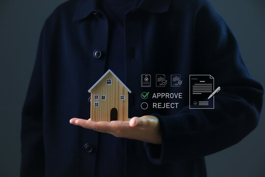 Real estate approval concept showing a hand holding a wooden house model with digital approve and reject icons, representing property investment decision, mortgage approval, financial evaluation.