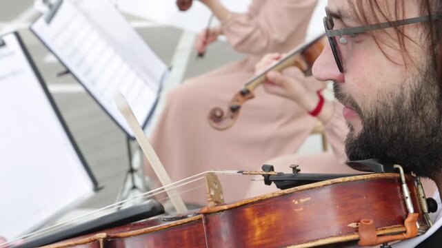 Close up of a bearded male musician in glasses playing viola at a wedding ceremony