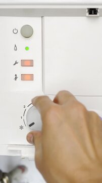 Close-up switching on the home boiler. The beginning of the heating season. The man's hand turns on the boiler and sets the temperature of heating and hot water