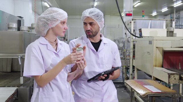 Two inspectors examining canned food and quality control in factory, food industry production line, technical team analyzing product standard, food processing facility, manufacturing quality food.