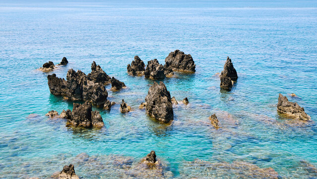 Dark volcanic rocks in crystal clear turquoise sea water in Scalea, Calabria, Italy. Scenic Mediterranean coastal landscape on a sunny day.