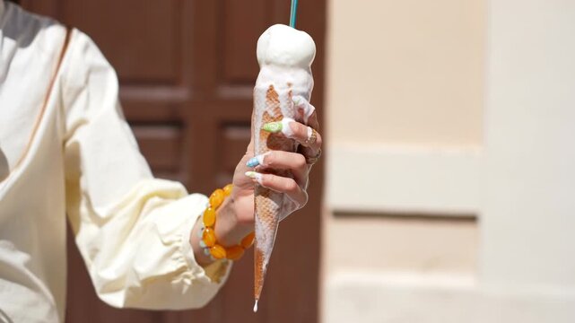 Vanilla ice cream cone melting and dripping down a woman's manicured hand on a hot sunny day. Close up on the sweet, cold dessert