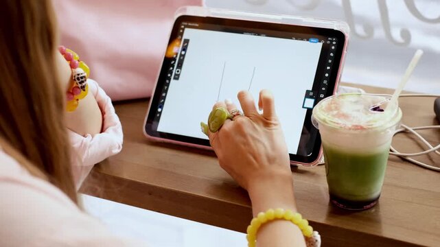 Creative female graphic designer drawing on a digital tablet in a cafe with a matcha green tea latte
