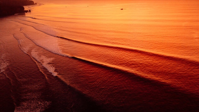 Golden sunset drone view of ocean waves rolling toward a tropical coastline