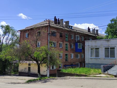 Old abandoned brick residential building with white extension and blue sky