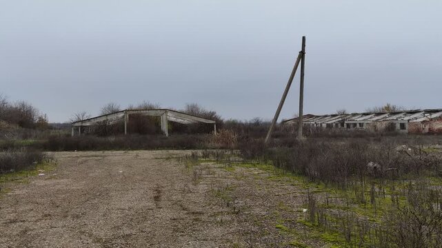Abandoned Soviet era farm concrete structure and leaning pole in a desolate field under gray sky