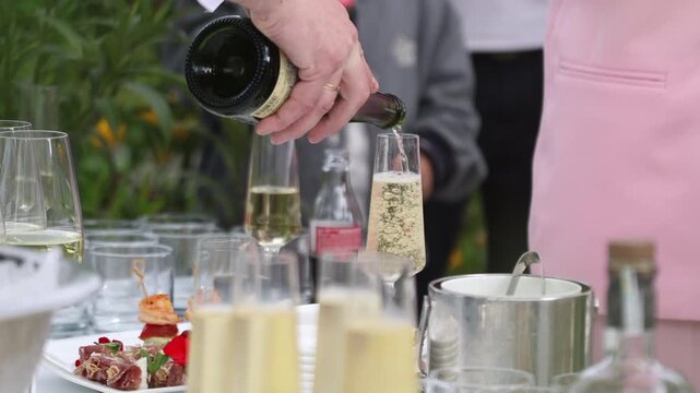 Close up of a waiter hand pouring champagne into flute glasses at an outdoor banquet