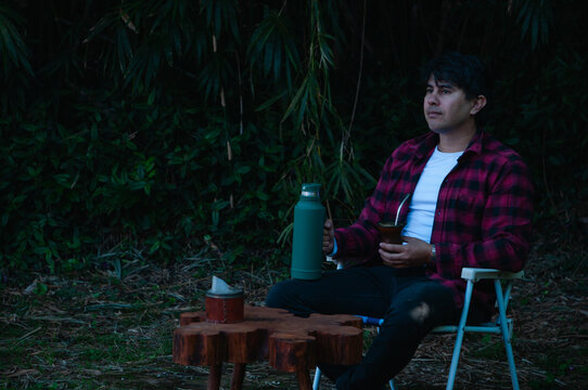 persona joven bebiendo mate en el jard&iacute;n o el parque. hombre contemplando el paisaje y con expresi&oacute;n de tranquilidad y calma