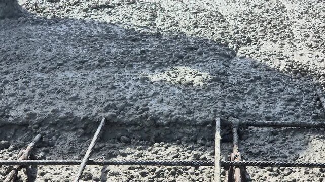 Fresh concrete pouring into the floor slab rebar reinforcement at a construction site, showing the cement texture filling the structure.