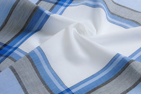 A close-up texture shot highlights the elegant folds and details of a white cotton handkerchief featuring blue and gray plaid borders.