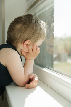 Curious little boy looking through a window at home. Childhood, curiosity, waiting, imagination, family life and cozy home lifestyle concept.