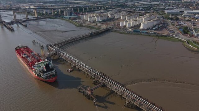 Oil terminal with oil storage tanks by the river Thames. Aerial view above the oil tanker ship on the river and oil pipes connected with the terminal. Dartford, UK, 05.31.2026