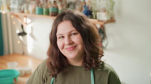 Caucasian potter in thoughtful pose in studio, apron on, clay preparation on table, soft natural light, shelves with jars and glazes, calm focused mood, ritual of craft, intimate portrait