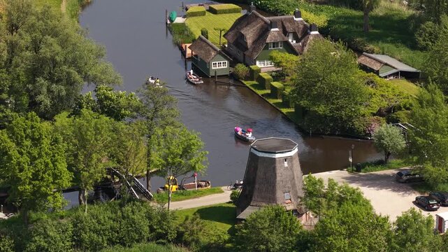 Tourists boating on canal in giethoorn village with traditional dutch windmill