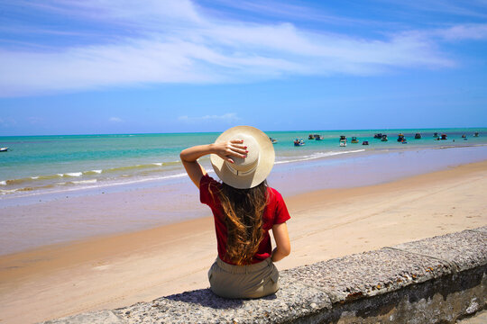 Holidays in Joao Pessoa, Brazil. Young woman sitting on wall enjoying sight of natural swimming pools with jangadas rafts in Joao Pessoa, Brazil.