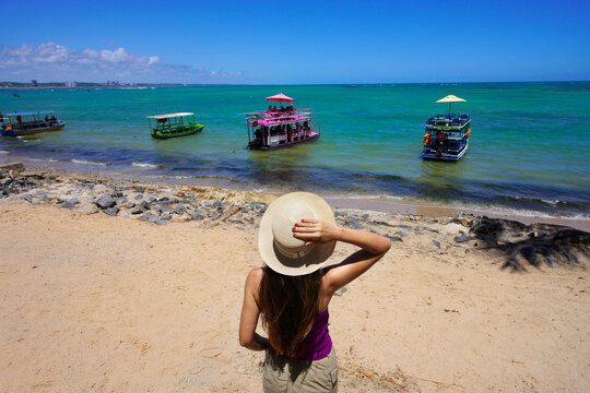 Vacation in Maceio, Brazil. Rear view of woman looking jangadas rafts going to natural swimming pools of Ponta Verde, Maceio, Brazil.