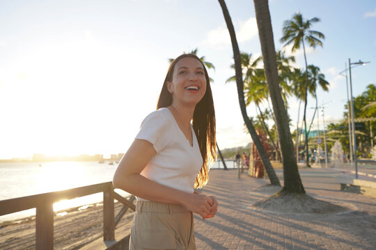 Smiling young woman walking on Maceio city promenade at sunset, Brazil