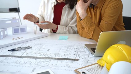 Architects collaborating on building design, analyzing blueprints and a scale model, planning...