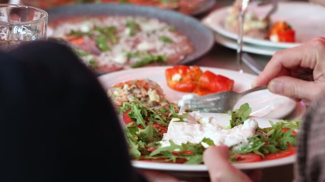 Close up of a person hand eating burrata salad with a fork at a restaurant banquet