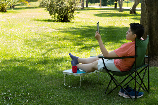 Young caucasian man relaxing outdoors with ebook in park