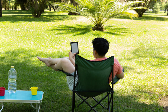 Young caucasian man reading ebook while relaxing in park