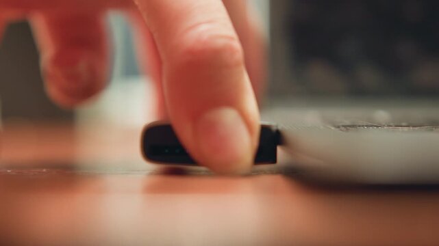 Person plugging key into computer. Individual carefully slots device into computer connection point. Detailed shot of hand gently inserting memory device into laptop port in personal workspace