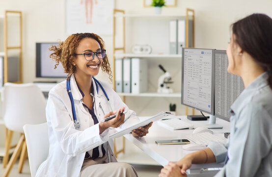 Doctor and patient consultation at clinic appointment. A smiling woman doctor leads a healthcare discussion, reviewing medical records on a computer screen. Clear patient centered care concept.