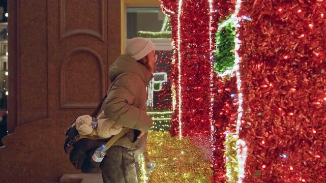 Woman enjoys city holiday lights. Evening scene with woman appreciating festive holiday illumination. Casual shot of woman savoring shimmering holiday lights along city street during evening