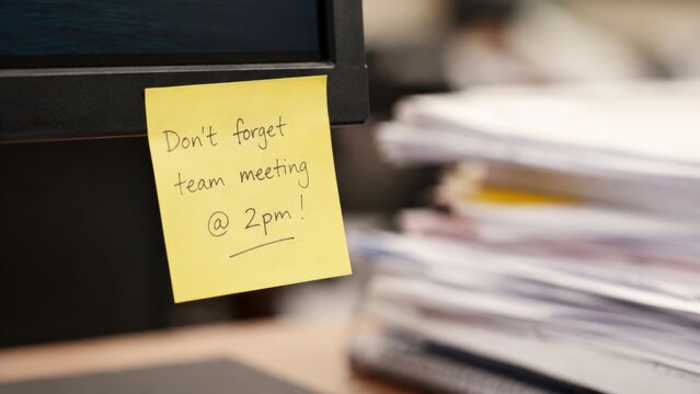 Yellow sticky note with meeting reminder on computer monitor.