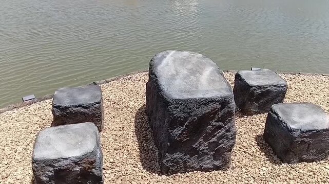 Tilt up shot of rustic stone benches built for relaxation near a small reservoir, with swan boats visible in the background.