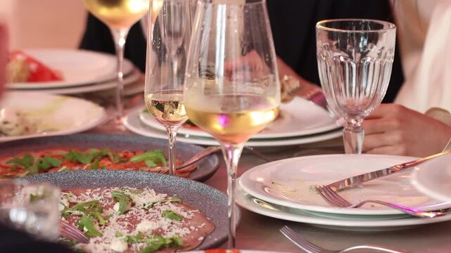 Selective focus on wineglasses with blurred hand serving food at a wedding reception table