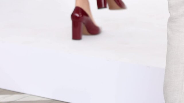 Close up of a woman walking in burgundy patent leather high heel shoes on wooden floor