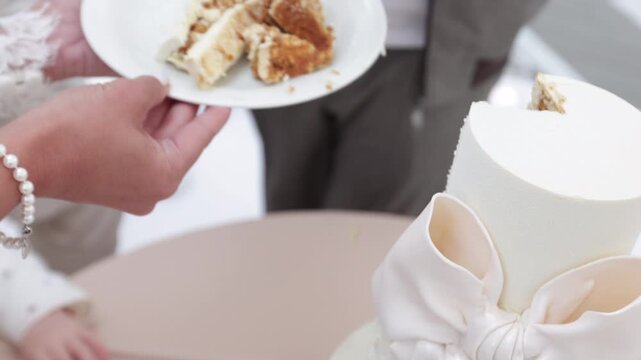 Close up of newlyweds hands cutting and serving wedding cake on a plate during reception