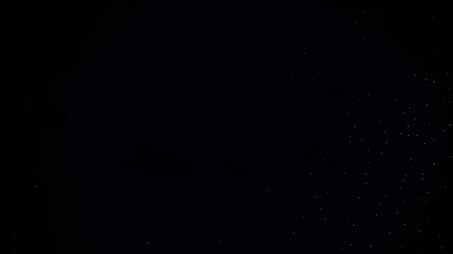 Bright white particles exploding outward in a dark void creating a dynamic motion video clip with glowing embers and shimmering light trails that expand rapidly across the deep black background screen