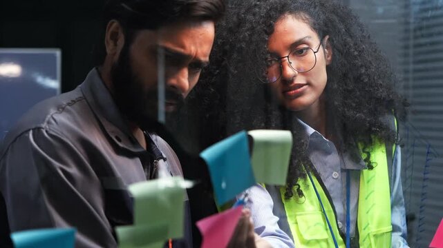 Diverse engineer team colleague analyzing construction project on office glass board, sticky note paper discussion work together for architectural building plan schedule