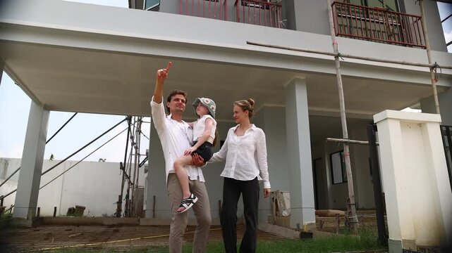 New house, caucasian family father, mother, and daughter look at their house that is under construction. They are imagining how they will live happily in this house (1)