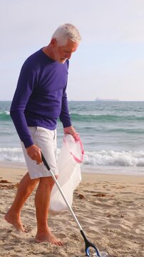 Mature 66 year old man picking up trash from a beach in Southern California. Vertical Video.