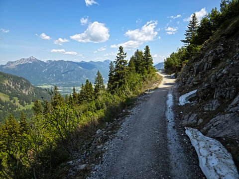 Austria, Idyllic mountain hiking trail beside snow fields surrounded by conifers under radiant blue skies on hahnenkamm mountain